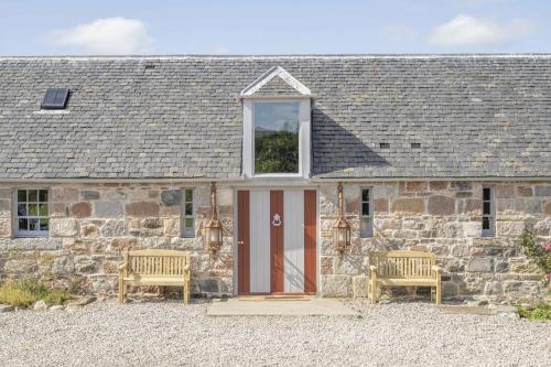 a stone cottage with a red door and two chairs at Drum Lodge in Nethy Bridge