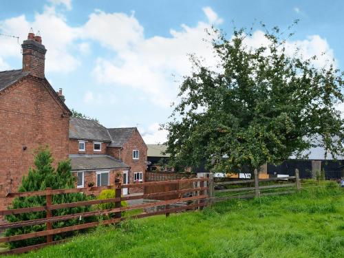 an old brick house with a wooden fence and a tree at Hillside Cottage in Hanmer