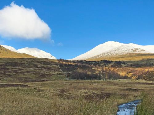a snowy mountain range with a stream in a field at Bridge Park in Killin