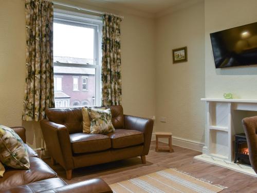 a living room with a leather couch and a window at Beachcomber Corner in Lytham St Annes