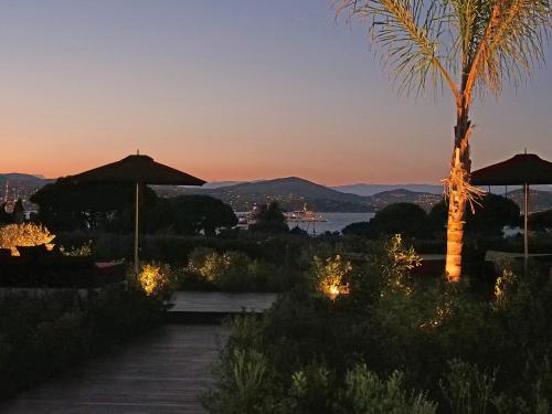 a pathway with umbrellas and a palm tree at sunset at Vyylla Private Resort in Saint-Tropez