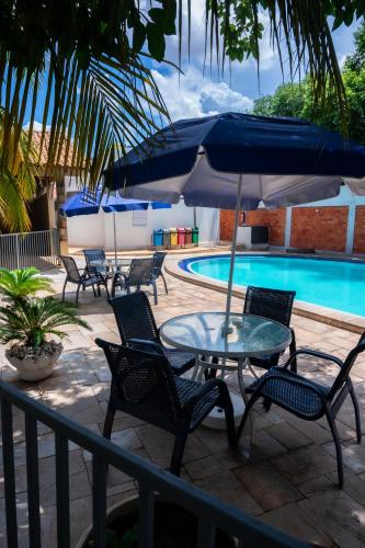 uma mesa e cadeiras com um guarda-sol ao lado de uma piscina em Delcas Hotel em Cuiabá