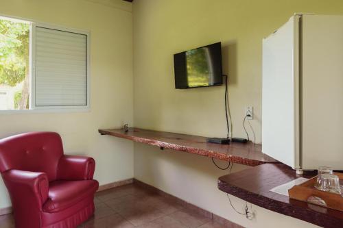 a room with a red chair and a television on a wall at Hotel Alto da Boa Vista in Analândia