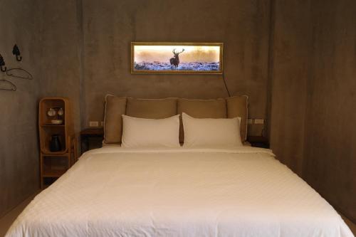 ein Bett mit weißer Bettwäsche und einem Bild an der Wand in der Unterkunft Lost in Memory in Sanxing Township