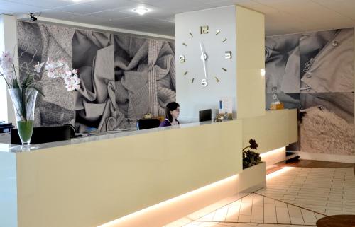 a woman sitting at a desk in an office with a clock on the wall at Hotel President in Prato