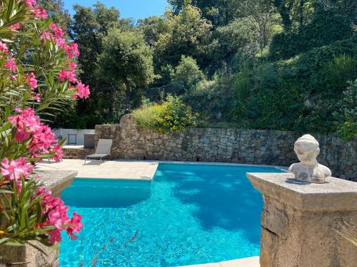 Una piscina en un patio con un muro de piedra y flores rosas. en Villa paisible avec piscine privée, en Auribeau-sur-Siagne