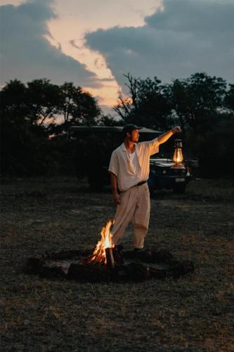 a man standing next to a fire in a field at Radisson Safari Hotel Hoedspruit in Hoedspruit