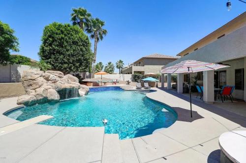 a swimming pool with a waterfall and an umbrella at Spacious 5BR Retreat Pool Grill 15 Min to Westgate in Litchfield Park