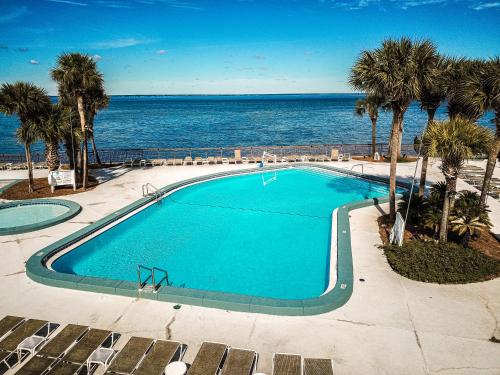 a swimming pool next to the ocean with palm trees at Bay Club of Sandestin in Destin