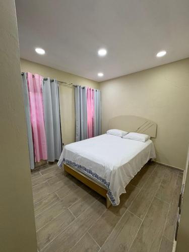 a bedroom with a bed with white sheets and pink curtains at Camiliahouse in San Pedro de Macorís