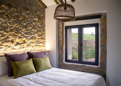 a bedroom with a stone wall and a bed with a window at Casa La Pascuala in Helgueras