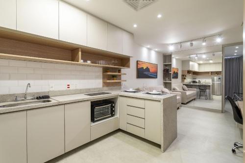 a kitchen with white cabinets and a living room at Apê com piscina e academia: Metrô 350m in Rio de Janeiro