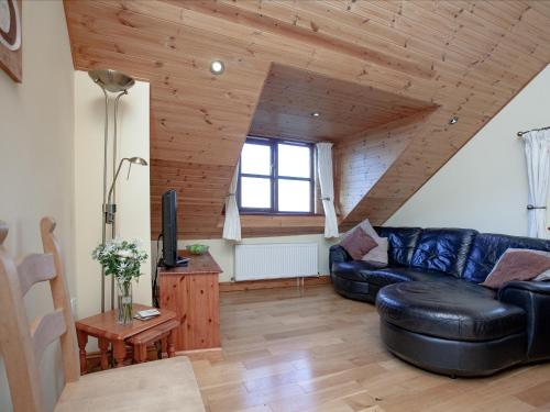 a living room with a black leather couch and wooden ceilings at The Old Mill House in Welcombe