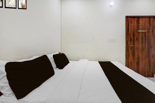 a white bed with black pillows and a wooden door at Super Hotel O IIM Road Lucknow in Lucknow