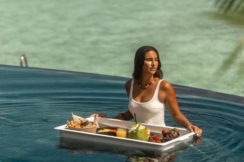 a woman sitting in the water with a tray of food at Sun Siyam Iru Fushi with Free Transfer in Manadhoo