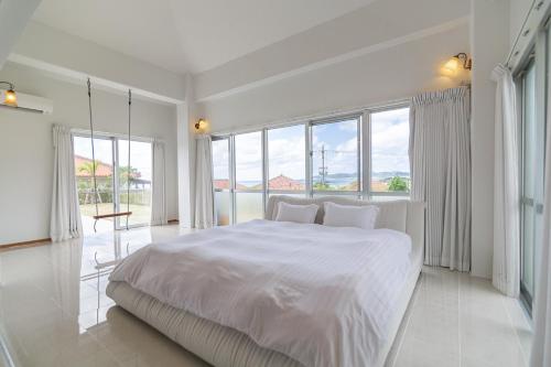 a white bedroom with a large bed and large windows at Sommelier Villa ISHIGAKI in Ishigaki Island