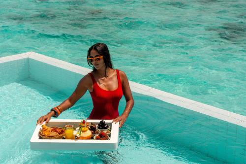 a woman in the water with a tray of food at Sun Siyam Iru Veli - 24 Hours Premium All-Inclusive with Free Transfers in Dhaalu Atoll