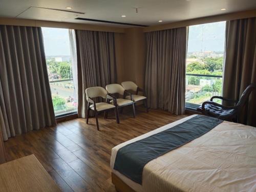 a hotel room with a bed and chairs and windows at Hotel Su-Casa in Bhavnagar