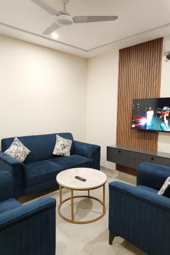a living room with blue couches and a tv at Luxe 1 Bedroom Apartment in Doha emporium B-17, Margalla views in Islamabad