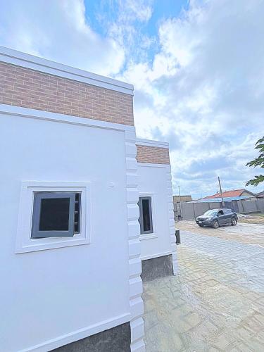 a white building with a car parked in a parking lot at Zeal City Dwellin in Loburo