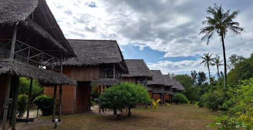 a row of houses with thatched roofs and palm trees at Kipepeo Beach and Village in Dar es Salaam