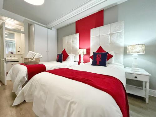 two beds in a bedroom with red and white at Coastal Hospitality - Beach Club 105 in Mossel Bay