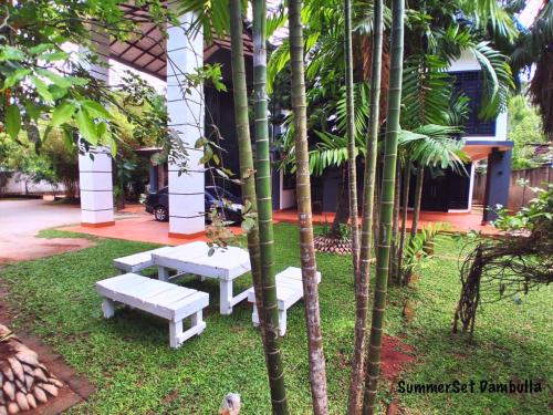 two white benches in front of a building with palm trees at SummerSet in Dambulla