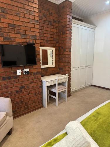 a bedroom with a brick wall with a table and a tv at Rivonia Garden Suites in Johannesburg