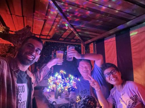 three people posing for a picture in front of a table with christmas lights at Napahong Treehouse นาป่าฮง Andromeda & Cassiopeia in Ban Pa Ha