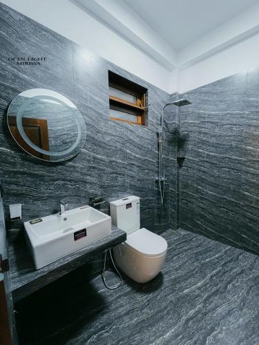 a bathroom with a toilet and a sink and a mirror at Ocean Light Mirissa in Mirissa