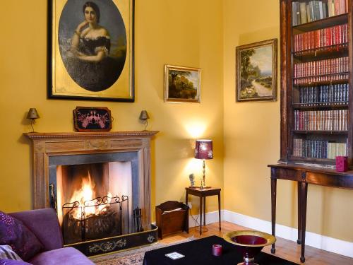 a living room with a fireplace and a book shelf with books at Lochside Garden House - S4484 in Town Yetholm