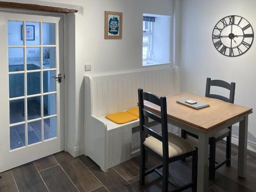a dining room with a table and a clock on the wall at The White Cottage in Gargrave