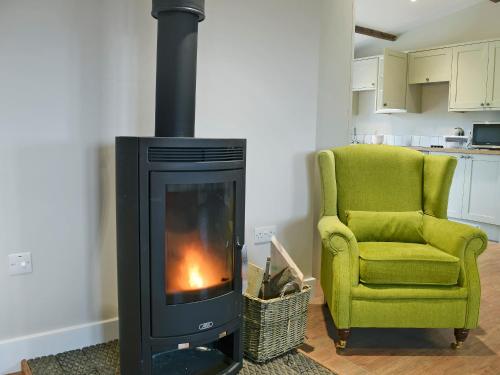 a living room with a stove and a green chair at Wagtail Cottage in Foxton