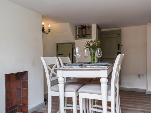 a white dining room table with white chairs and a vase of flowers at Drapers Cottage in Foxton