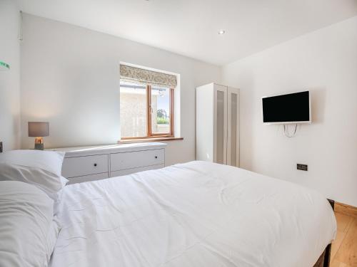 a white bedroom with a white bed and a tv at Sir A Wel in Llanerchymedd