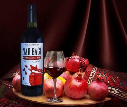 a bottle of red wine next to a glass and pomegranates at NovART Gallery & Sea Hotel in Sumqayyt