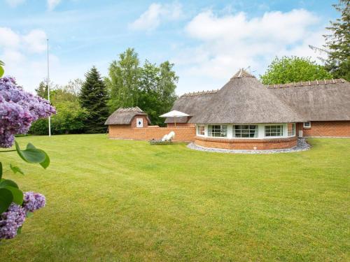 a large yard with a building with a thatch roof at 12 person holiday home in Væggerløse in Marielyst