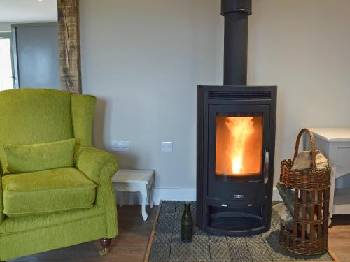 a living room with a fireplace and a green chair at Waxwing Cottage in Foxton