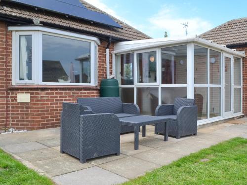 a conservatory with two chairs and a bench in front at Sea La Vie in Mundesley