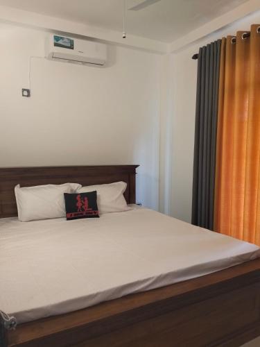 a bedroom with a large bed with an orange curtain at Rose Apartment in Kadawata
