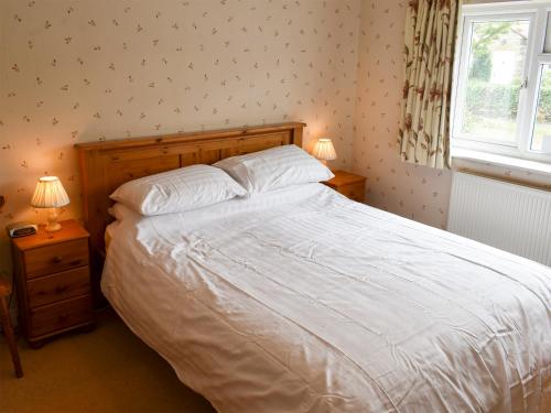 a bedroom with a bed with white sheets and a window at Blacksmiths Cottage in Gillamoor