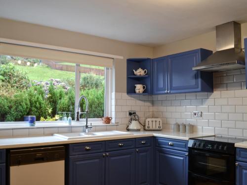 a blue kitchen with a sink and a window at Devana Croft in Tarbert
