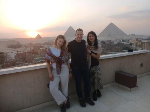 three people standing on a ledge in front of the pyramids at Happy Day Pyramids View Hotel in Cairo