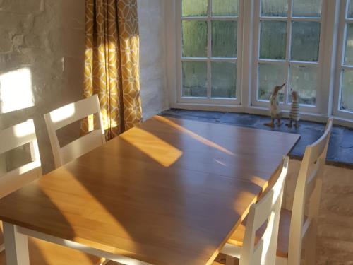 a wooden table with two chairs and a cat looking out the window at Dovecote-Tnq in Camelford