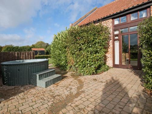 a brick house with a green trash can and a bench at Bay - E4482 in Ludham