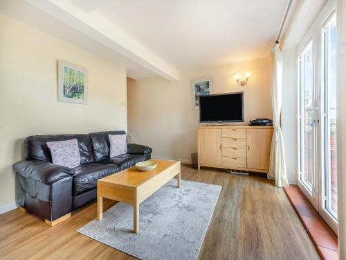 a living room with a black leather couch and a tv at The Cottage in Fairlight