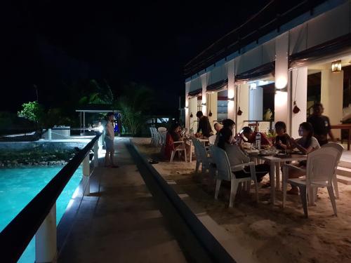 a group of people sitting at a table by a pool at night at Lagoon View in Bodufolhudhoo