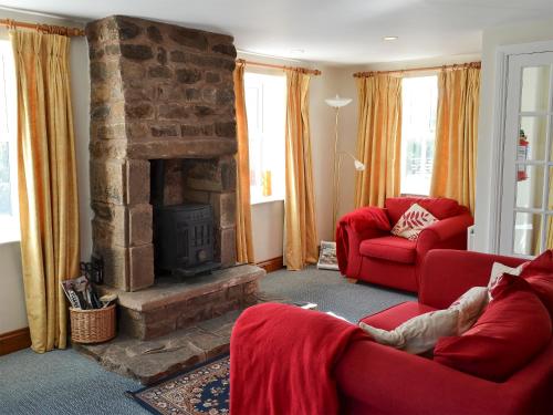 a living room with two red couches and a fireplace at Felbridge Cottage in Bardon Mill