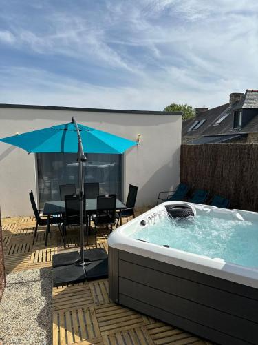 ein Whirlpool auf einer Terrasse mit einem Tisch und einem Sonnenschirm in der Unterkunft Le Nid Des Grèves avec jacuzzi in Langueux