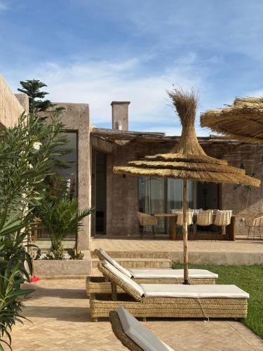 a patio with a straw umbrella and chairs and a table at Charming Beldi villa with pool in Sidi Kaouki